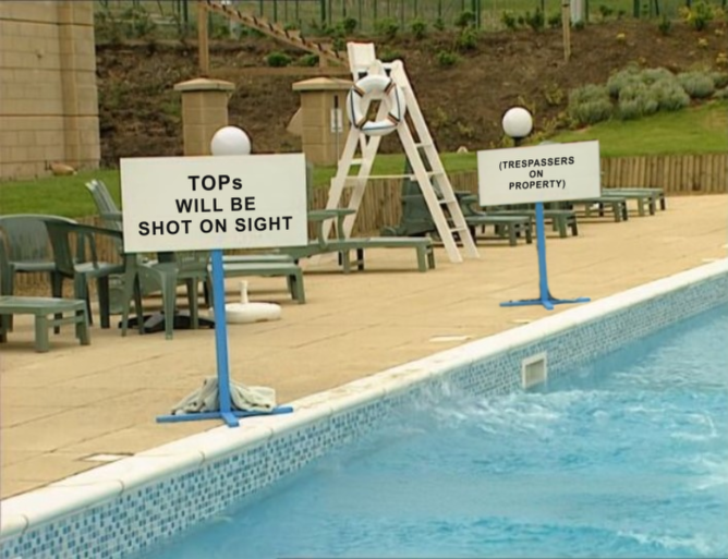 Two signs beside a swimming pool. The one nearest the viewer reads: "TOPs WILL BE SHOT ON SIGHT." The sign further away clarifies that 'TOP' is an acronym: "TRESPASSERS ON PROPERTY."